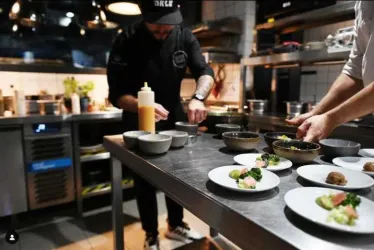In einer modernen Küche bereiten Köche verschiedene Gerichte vor. Auf dem Tisch stehen mehrere Schalen und Teller mit sorgfältig angerichteten Speisen.