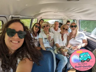 Eine Gruppe von Frauen sitzt in einem VW-Bus und lächelt in die Kamera. Alle genießen die fröhliche Stimmung.