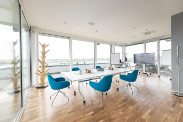 Ein modernes Besprechungszimmer mit großen Fenstern und Blick auf das Wasser. Blaues Mobiliar und ein großer Tisch schaffen eine einladende Atmosphäre.