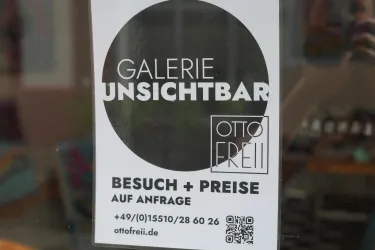 Ein Schild der Galerie Unsichtbar, das Informationen zu Besuchen und Preisen bereitstellt. Kontaktinformationen sind ebenfalls aufgeführt.