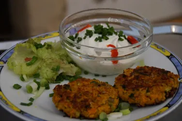 Zwei knusprige Gemüsefrikadellen auf einem Teller, neben einem Salat aus Kopfsalat und Frischkäse mit roten Chili-Streifen. Das Gericht ist mit frischen Schnittlauchstückchen garniert.