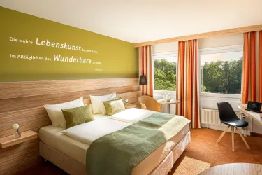 Ein modernes Hotelzimmer mit zwei Betten und hellen Farben. Große Fenster bieten einen Blick auf die Natur.