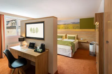 Ein modernes Hotelzimmer mit einem Doppelbett, einem Schreibtisch und einem großen Fenster. Die Einrichtung ist in warmen Farben gehalten und vermittelt eine gemütliche Atmosphäre.