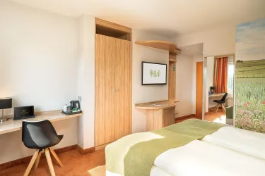 Ein modernes Hotelzimmer mit zwei Betten und einem Schreibtisch. Der Raum ist hell und freundlich gestaltet, mit einem schönen Blick auf die Natur.