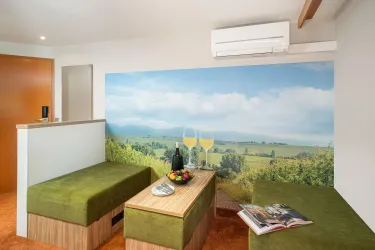 Ein modernes Zimmer mit grünen Sitzbänken und einem Tisch. Im Hintergrund ist ein Panorama mit einer schönen Landschaft und zwei Gläsern mit Getränken zu sehen.