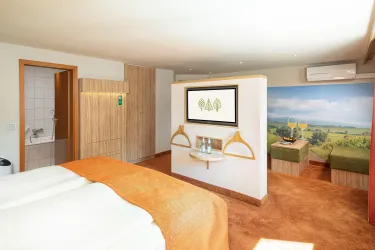 Ein modernes Zimmer mit einem komfortablen Bett und warmen Farben. Im Hintergrund ist eine schöne Landschaft abgebildet und es gibt einen TV-Bereich.