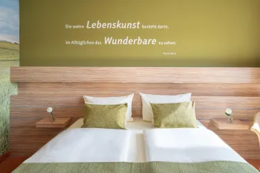 Ein modernes Schlafzimmer mit einem Doppelbett und einer Holzverkleidung. An der Wand steht ein Zitat über Lebenskunst.