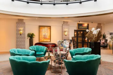 Ein elegantes Hotel-Lobby mit stilvollen, grünen Sesseln und einem modernen Tisch. Im Hintergrund sind Kunstwerke und Pflanzen zu sehen, die eine entspannte Atmosphäre schaffen.