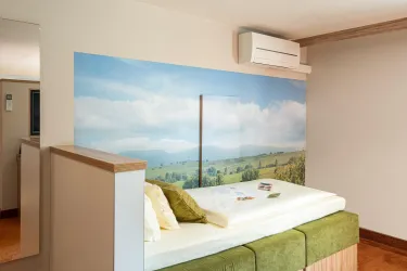 Ein modernes Zimmer mit einem Bett und einer schönen Wandmalerei, die eine Landschaft mit Himmel und Hügeln zeigt. Es gibt helle Farben und eine gemütliche Atmosphäre.