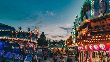 Ein lebhaftes Jahrmarkt mit bunten Fahrgeschäften und Lichtern. Der Himmel ist düster und die Atmosphäre ist festlich.