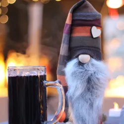 Ein fröhlicher Weihnachtszwerg steht neben einem großen Bierglas. Die Umgebung wirkt festlich und einladend.