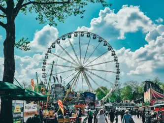 Ein Riesenrad steht im Mittelpunkt eines lebhaften Festplatzes. Der Himmel ist klar und voller interessanter Wolken.