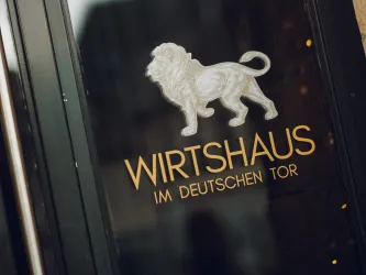 Ein einladendes Wirtshaus mit einem Löwenlogo. Der Name „Wirtshaus im Deutschen Tor“ ist elegant gestaltet.