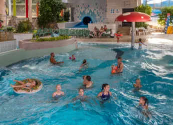 Ein indoor Wasserpark mit vielen Schwimmern. Kinder spielen im Wasser und auf Rutschen, während Erwachsene entspannen.
