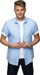Ein junger Mann trägt ein hellblaues Hemd und ein weißes T-Shirt. Er schaut direkt in die Kamera und hält das Hemd leicht geöffnet.