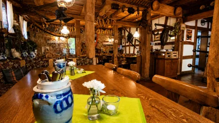 Eine rustikale Gaststube mit Holzdekor und warmem Licht. Auf dem Tisch stehen Blumenvasen und Dekorationen.