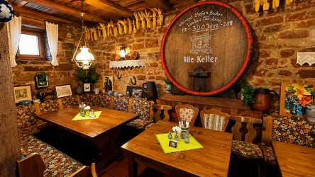 Ein gemütliches Restaurant mit Holztischen und bunten Stoffstühlen. An der Wand hängt ein großes Weinfass, das der Raumgestaltung einen rustikalen Charme verleiht.