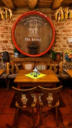 Ein gemütliches Restaurant mit Holztisch und Stühlen. Im Hintergrund steht ein großes Weinfass und die Wände sind mit Steinmauern dekoriert.