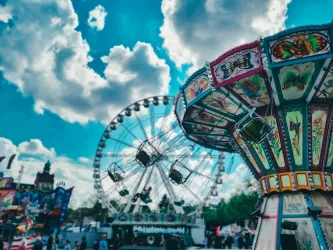 Ein bunter Jahrmarkt mit einem Riesenrad und einem Karussell. Helle Wolken schweben über dem lebhaften Vergnügungspark.