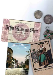 Ein historisches Geldschein mit der Aufschrift "Zehn Millionen Mark" und mehrere alte Münzen sind abgebildet. Daneben liegen zwei Karten mit Stadtansichten und traditionellen Motiven.