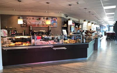 Ein einladendes Café mit einer Theke, die verschiedene Backwaren und Desserts präsentiert. Die Atmosphäre ist hell und freundlich, ideal für entspannte Stunden.