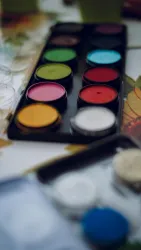 Eine Palette mit verschiedenen Farbtönen, darunter Rot, Grün, Blau und Gelb. Sie liegt auf einem bunten Tisch mit einer kreativen Umgebung.