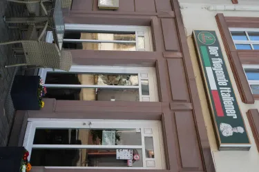 Ein Restaurant mit dem Namen „Der fliegende Italiener“. Die Fassade ist hell und freundlich mit Tischen im Außenbereich.