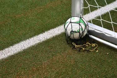 Ein Fußball liegt in der Ecke eines Fußballtors auf dem Spielfeld. Das Netz ist teilweise um den Ball gewickelt.