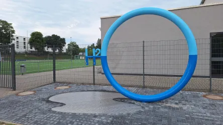 Ein großes blaues O, eigebettet in H2O bildet einen Blickfang am Sportplatz West. Zwei Wasserspender des Gebäudemanagement Landau bieten kostenfreies Trinkwasser an. Auf Knopfdruck sprudelt das Wasser aus dem Brunnen. Man kann entweder direkt etwas trinken oder seine Trinkflasche befüllen.