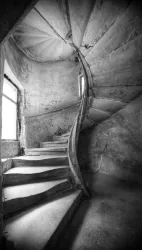 Eine gewundene Treppe in einem alten Gebäude. Die Wände sind rau und das Licht fällt durch ein Fenster.