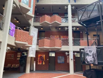 Ein Innenhof mit mehreren Etagen, der mit Kunstwerken dekoriert ist. Die Wände bestehen aus Backstein, und es gibt Balkone und Sitzgelegenheiten.