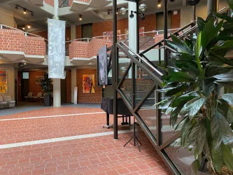 Ein moderner Innenraum mit roten Ziegelwänden und einer Treppe aus Glas. Im Hintergrund sind Pflanzen und Kunstwerke zu sehen.