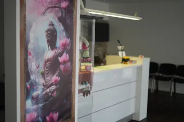 Ein ruhiger Empfangsbereich mit einer Buddha-Darstellung und pinken Lotusblumen. Der moderne Schreibtisch und die Stühle im Hintergrund sorgen für eine einladende Atmosphäre.