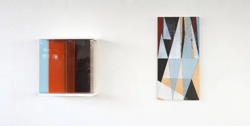 Zwei Kunstwerke an einer weißen Wand. Links ein farbiger Kasten und rechts ein geometrisches Gemälde mit verschiedenen Farben.