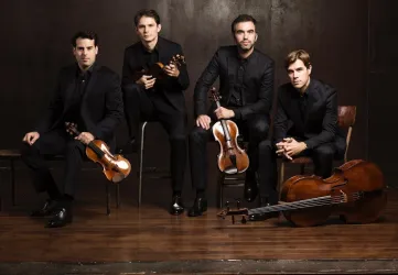Eine Gruppe von vier elegant gekleideten Musikern sitzt mit ihren Streichinstrumenten auf unterschiedlich hohen Stühlen. Sie strahlen eine musikalische Eleganz aus.