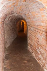 Ein schmaler, gemauerter Tunnel mit beleuchteten Wänden. Der Boden ist uneben und die Atmosphäre wirkt geheimnisvoll.