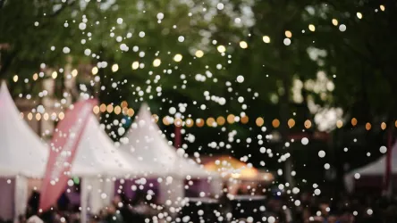 Ein festliches Ambiente mit glitzernden Lichtern und Zelten. Im Vordergrund sind viele helle Punkte zu sehen, die eine festliche Stimmung erzeugen.