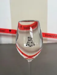 Ein Weinglas mit der Aufschrift "SOUPE SALON" steht auf einem Tisch. Im Hintergrund sind rot-weiße Warnbänder sichtbar.