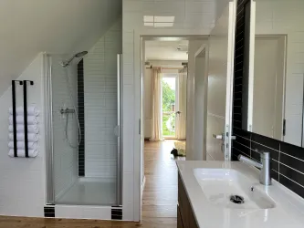 Modernes Badezimmer mit Dusche, WC und Badewanne, mit Blick ins zweite Schlafzimmer.