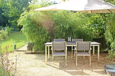 Essbereich im Freien mit einem Tisch und 4 Stühlen unter einem schattenspendenden Sonnenschirm, umgeben von üppigem Grün und einem ruhigen Garten.