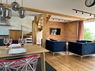 Offenes Wohn-Esszimmer, mit 2 Couchen. Es gibt eine offene Treppe und große Fenster, die viel Licht hereinlassen.