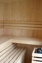 Heller Saunaraum mit Holzverkleidung und Sitzbänken aus hellem Holz. Der Raum vermittelt eine entspannende und gemütliche Atmosphäre.