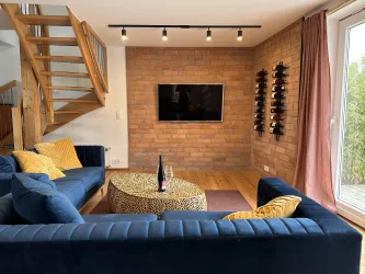 Ein modernes Wohnzimmer mit einer blauen Couch und einem runden Tisch. An der Wand hängt ein Fernseher, während Weinfässer zur Dekoration dienen.