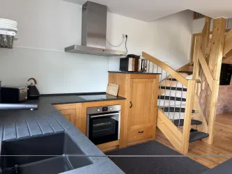 Moderne Küche mit Holzschränken, Spülmaschine und Herd, die Treppe führt zum oberen Stockwerk.