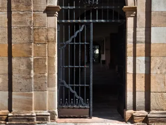 Ein historisches Tor aus Schmiedeeisen mit steinernen Wänden. Der Blick führt in einen dunklen, einladenden Innenraum.