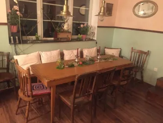 Ein einladender Essbereich mit einem großen Holztisch und Holzstühlen. Auf dem Tisch liegt eine grüne Dekoration und Kerzen, während Pflanzen das Fenster verschönern.