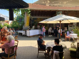 Ein einladender Außenbereich mit Tischen und Sonnenschirmen. Menschen genießen die Atmosphäre in einem geschäftigen Garten.
