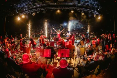 Ein lebhaftes Konzert mit einem großen Orchester auf der Bühne. Funkelnde Feuerwerkskörper sorgen für eine festliche Atmosphäre.