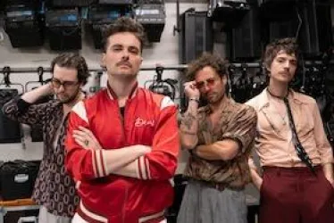 Vier Männer stehen mit unterschiedlichen Posen und coolen Outfits vor einer Kulisse von Lichttechnik. Sie wirken kreativ und stylisch.
