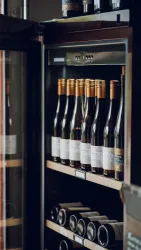 Eine Weinschranks mit mehreren Flaschen Wein. Die Flaschen sind ordentlich angeordnet und haben verschiedene Etiketten.